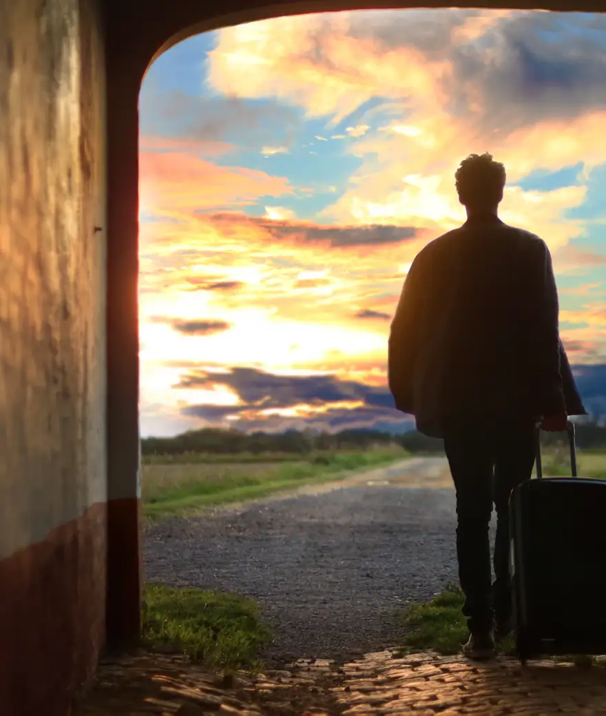 Viajante com mala em frente a uma porta aberta para o campo